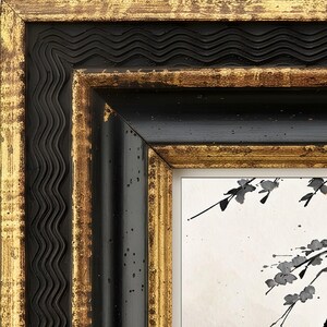 May include: A decorative picture frame featuring a multi-layered design with a wavy black outer edge, a smooth black inner border, and distressed gold leaf accents on the raised surfaces. The frame surrounds a white print with black ink branches.