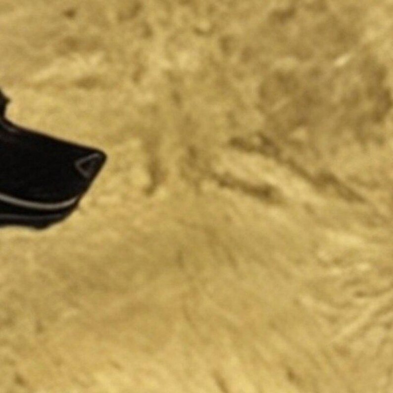 May include: A black, angular object with a smooth, dark surface and a distinct white line detail along its edge, positioned against a textured, golden-yellow background that fills the majority of the frame.