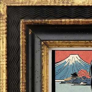 May include: A rectangular picture frame with a black and gold finish featuring a wavy inner border and a flat outer edge. The frame surrounds a print depicting a mountain with a snow-capped peak against a red sky, blue water, and foliage.