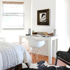 May include: A framed wall art piece featuring a black silhouette of a cat perched on a tree branch against a light background, enclosed in a dark, ornate, multi-layered frame with gold accents, hanging on a plain white wall above a white desk.