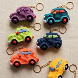 Peut inclure: Six porte-clés en forme de voiture crochetés en violet, bleu sarcelle, vert citron, bleu marine, orange et jaune. Chaque voiture possède une chaîne et un anneau en métal doré, des roues noires et des fenêtres bleu clair ou rouges.