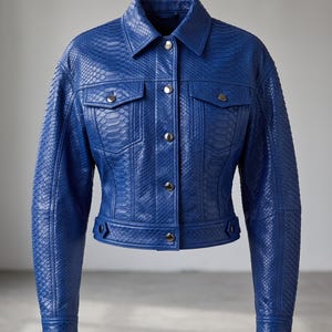 Puede incluir: Una chaqueta de color azul vibrante con un patrón texturizado de piel de serpiente. La prenda incluye un cuello clásico, mangas largas con puños abotonados, dos bolsillos en el pecho con solapas y un cierre frontal de botones metálicos.