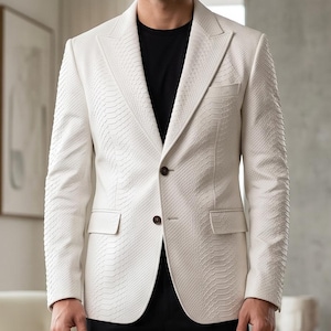 May include: A white blazer with a textured snakeskin pattern, featuring a notched lapel, two dark buttons, and two flap pockets. The blazer is worn over a plain black t-shirt and paired with black trousers, creating a high-contrast ensemble.