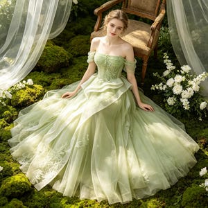 Könnte beinhalten: Ein bodenlanges, salbeigrünes Kleid mit schulterfreiem Ausschnitt, einem strukturierten Oberteil mit zarter Blumenstickerei und einem voluminösen Rock aus mehreren Lagen transparentem Tüll mit aufwendigen Spitzenapplikationen.