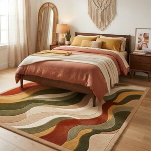 May include: A rectangular area rug featuring a wavy, multi-colored pattern in shades of terracotta, olive green, mustard yellow, and cream. The rug has a textured, tufted surface with a thick border and is positioned under a wooden bed frame.