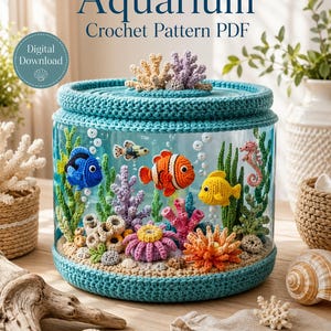 Puede incluir: Un patrón de ganchillo en PDF de descarga digital titulado Aquarium que muestra un frasco de vidrio lleno de vida marina tejida, incluyendo un pez cirujano azul, pez payaso, pez amarillo, caballito de mar y corales coloridos sobre arena.
