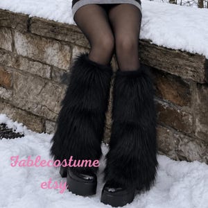 May include: A pair of black faux fur leg warmers worn over sheer black tights and black platform boots. The text Fablecostume etsy is overlaid in pink on the lower left side of the image. The leg warmers feature long, shaggy black synthetic fibres.