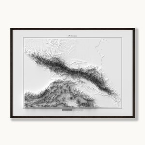 May include: A framed topographic map titled The Caucasus, featuring a high-contrast greyscale relief of the mountain range. The print displays detailed elevation shading, a thin black border, and a scale bar at the bottom centre.