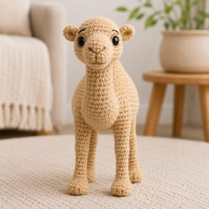May include: A beige crochet camel stuffed animal featuring a textured yarn construction, a prominent hump, four legs, small ears, and two round black plastic eyes. The camel is standing upright and has a detailed stitched nose and mouth area.