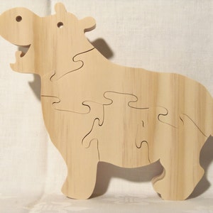 May include: A wooden puzzle of a hippopotamus, made of multiple interlocking pieces. The puzzle is unpainted and has a natural wood finish.
