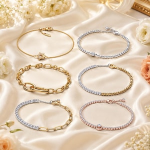 Peut inclure: Six bracelets disposés sur un tissu satiné. En haut à gauche : chaîne dorée avec une breloque étoile. En haut à droite : chaîne perlée argentée. Milieu gauche : chaîne à maillons ovales dorés. Milieu droite : chaîne perlée mixte or et argent. En bas à gauche : chaîne argentée avec maillons et pierres. En bas à droite : chaîne perlée en or rose avec une pierre centrale.