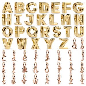 Pode incluir: Uma coleção de berloques de alfabeto em metal dourado com letras maiúsculas de A a Z nas linhas superiores e berloques menores de letras minúsculas em cursivo com argolas integradas nas linhas inferiores, dispostos em uma grade.