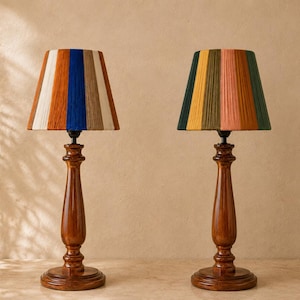 May include: Two table lamps with dark brown wooden bases and pleated fabric shades. The left lamp shade features vertical stripes in white, orange, blue, and tan. The right lamp shade features vertical stripes in dark green, yellow, and pink.