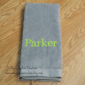 May include: Gray towel with a green embroidered name "Parker" and a gold ring attached.