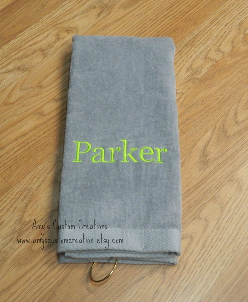 May include: Gray towel with a green embroidered name "Parker" and a gold ring attached.