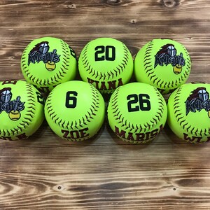 May include: Seven lime green softball with black stitching and black embroidered text. The text on the balls reads "Knights", "20", "Tiana", "6", "Zoe", "26", "Marisa", and "Wilma".