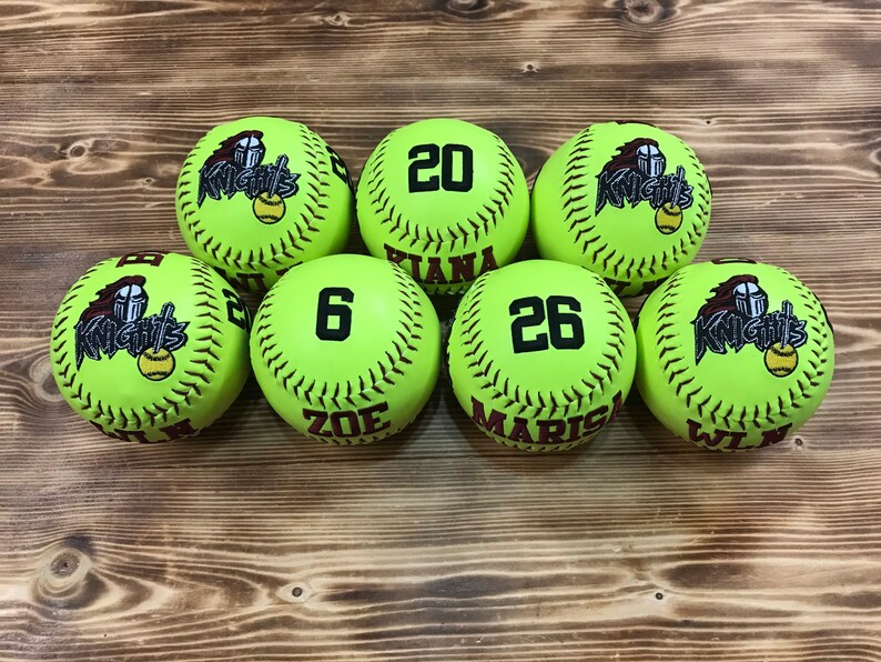 May include: Seven lime green softball with black stitching and black embroidered text. The text on the balls reads "Knights", "20", "Tiana", "6", "Zoe", "26", "Marisa", and "Wilma".