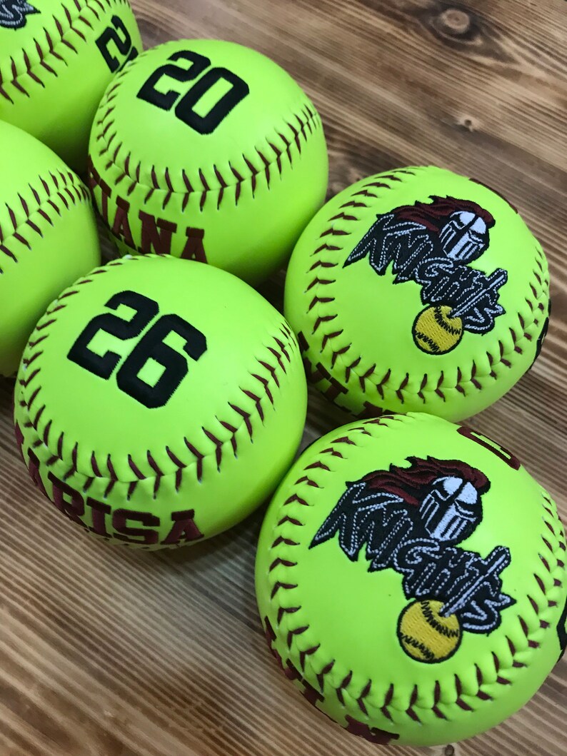May include: Five yellow softball with brown stitching.  Three of the softballs have a black number, 20, 26, and 20. Two of the softballs have a brown embroidered logo that says "Knights".