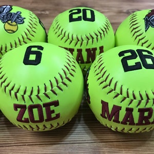 May include: Six lime green softball with maroon stitching. The softballs are personalized with names and numbers. The names are Zoe, Maris, and the numbers are 6, 20, and 26.