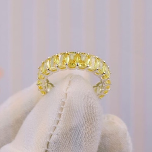 Könnte beinhalten: Ein silberfarbener Eternity-Ring mit einer durchgehenden Reihe rechteckiger, im Baguette-Schliff geschliffener gelber Edelsteine. Der Ring verfügt über eine Metallfassung, die jeden Stein sicher hält und für ein gleichmäßiges, leuchtend gelbes Aussehen sorgt.