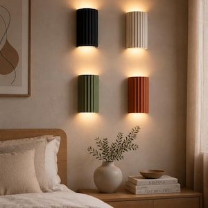 Peut inclure: Quatre appliques murales semi-cylindriques à texture nervurée verticale, disposées en grille deux par deux. En haut à gauche, une noire, en haut à droite, une blanc cassé, en bas à gauche, une vert sauge et en bas à droite, une terre cuite.