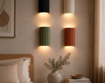 May include: Four semi-cylindrical wall sconces with vertical ribbed textures, mounted in a two-by-two grid. The top left is black, top right is off-white, bottom left is sage green, and bottom right is terracotta. Each emits warm light.