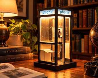 May include: A miniature black telephone booth lamp with a square base and illuminated panels featuring the word phone in blue text. The interior contains a small white shelf and a wall-mounted telephone handset, casting a warm glow from within.