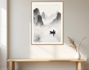 Op de afbeelding: Een ingelijste wandkunstprint met een landschap in zwart-wit inktwasstijl. De scène toont een eenzame figuur in een kleine boot op kalm water, omringd door mistige, torenhoge bergtoppen op de achtergrond, gepresenteerd in een lichthouten lijst.