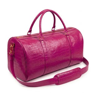 Puede incluir: Un bolso de viaje color magenta vibrante con un patrón texturizado de piel de cocodrilo. El bolso incluye dos asas superiores, un cierre de cremallera dorado y una correa de hombro desmontable con una sección acolchada y herrajes dorados.