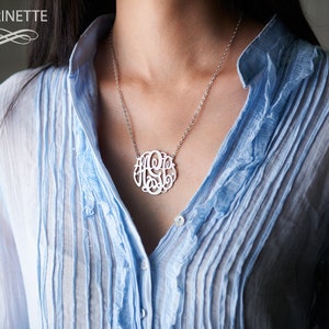 Puede incluir: Un collar de plata con un colgante circular que presenta las letras "A.S.E." en una fuente de escritura. El collar lo lleva una persona con una camisa azul claro.