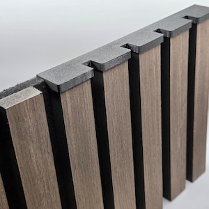 May include: A wall panel featuring vertical brown wood-look slats attached to a black felt backing. The top edge is finished with a black plastic trim piece that caps each individual slat, creating a clean, uniform edge along the top of the panel.
