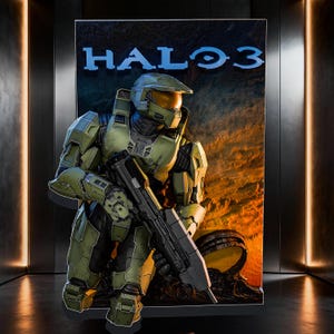 May include: A vertical display board featuring the Halo 3 logo in blue text at the top. The graphic depicts a soldier in green armored plating with a gold visor, holding a dark gray rifle. The background shows a rocky, orange-lit landscape.
