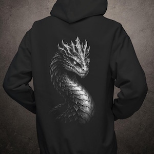 May include: A black hooded sweatshirt featuring a detailed, monochromatic graphic print on the back. The design depicts a serpent-like dragon with intricate scales and a crown-like crest on its head, rendered in shades of grey and white.