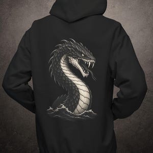 May include: A black hooded sweatshirt featuring a large graphic on the back. The design depicts a detailed, dark-scaled serpent with sharp fangs and a forked tongue emerging from stylised ocean waves in shades of grey, white, and black.