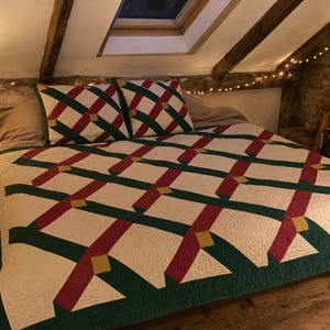 Könnte beinhalten: Eine gesteppte Tagesdecke und zwei passende quadratische Kissen mit einem geometrischen Gittermuster in Creme, Dunkelgrün und Kastanienbraun, akzentuiert durch kleine goldene rautenförmige Einsätze an den Kreuzungspunkten der Stoffstreifen.
