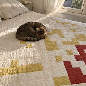 May include: A cream-colored quilt featuring a grid pattern with scattered yellow and red square blocks. A brown tabby cat is curled into a ball on the surface of the quilt. The fabric has a visible quilted texture with stitching throughout the design.