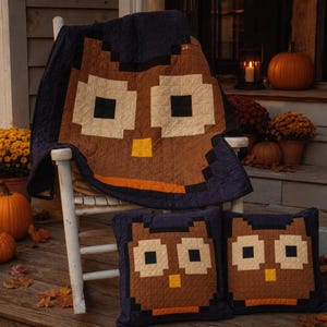 May include: A quilt and two matching square pillows featuring a pixelated owl design. The owl motifs are rendered in shades of brown, cream, and black with yellow beaks and orange accents, all set against a dark navy blue background fabric.