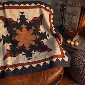 May include: A quilted blanket featuring a geometric star pattern in navy blue, rust orange, and cream white. The design includes a central star motif surrounded by smaller triangular shapes and a wide border with a sawtooth edge in navy and rust.