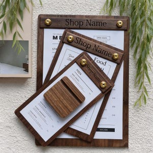 May include: Three dark wood menu boards of varying sizes, each featuring a horizontal wooden bar secured by two gold-toned metal screws. The text "Shop Name" is engraved on each bar. A small, square wooden block rests on the smallest menu board.