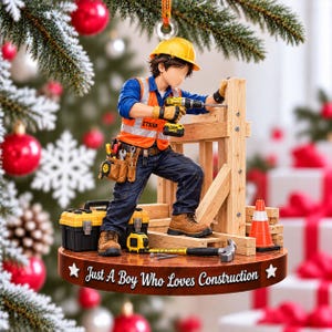 May include: A construction worker figurine ornament wearing a yellow hard hat, orange safety vest with the name Ethan, blue shirt, and dark pants. The figure holds a power drill on a wooden frame with a toolbox, hammer, and traffic cone.