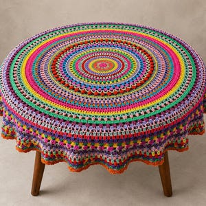 Può includere: Una tovaglia rotonda all'uncinetto multicolore con motivi circolari concentrici in tonalità vivaci di rosa, giallo, blu, verde, viola e arancione. Il tessuto presenta un bordo smerlato testurizzato ed è drappeggiato su un tavolino in legno.