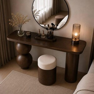 Peut inclure: Une console en bois brun foncé avec un plateau rectangulaire lisse, soutenue par deux pieds distincts : l'un composé de sphères empilées et l'autre d'un cylindre plein. Un tabouret cylindrique assorti à assise crème est placé devant.