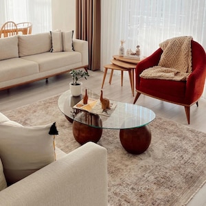 Puede incluir: Una sala de estar con un sofá beige con un cojín a rayas, un sillón rojo con una manta de punto beige y una mesa de centro con tapa de cristal y dos bases esféricas de madera. Una pequeña planta y dos figuras de animales de madera están sobre la mesa.