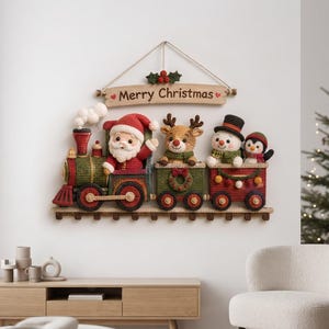 May include: A crocheted wall hanging featuring a train with Santa Claus, a reindeer, a snowman, and a penguin in the carriages. Above the train, a wooden sign reads Merry Christmas with holly accents. The train is red, green, and brown.