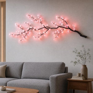Peut inclure: Une branche décorative fixée au mur ornée de nombreuses petites fleurs de cerisier rose lumineuses. La branche présente une finition sombre et texturée rappelant l'écorce et s'étend horizontalement, diffusant une lumière douce.
