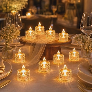 Può includere: Un set di dieci piccoli portacandele in vetro trasparente con motivo a diamante, ciascuno contenente una candela LED luminosa. Tre portacandele sono rialzati su un piedistallo in legno drappeggiato, sette sono disposti sul tavolo.