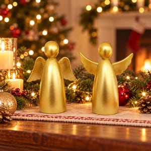 May include: Two gold-colored angel figurines with smooth, rounded heads and outstretched wings. The figures have a solid, conical body shape and a metallic finish, standing upright as decorative ornaments for a holiday display.