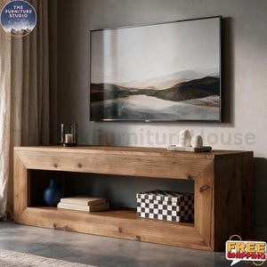 May include: A rectangular wooden media console with a natural grain finish and a large open storage shelf. The shelf contains a blue vase, two stacked books, and a black and white checkered box. A landscape painting hangs on the wall above.