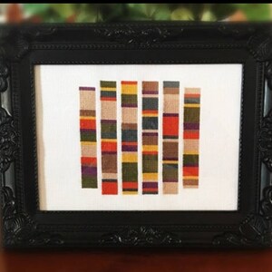 May include: A framed cross-stitch design featuring a series of colorful stripes in various shades of red, orange, yellow, green, blue, purple, and brown. The stripes are arranged in a vertical pattern, creating a visually appealing and modern design.