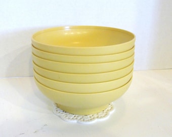 Puede incluir: Una pila de seis cuencos de color amarillo pálido. Los cuencos son redondos con un borde ligeramente ensanchado y un diseño acanalado en los lados. Están sobre un tapete blanco y de encaje. Los cuencos son de color amarillo claro.